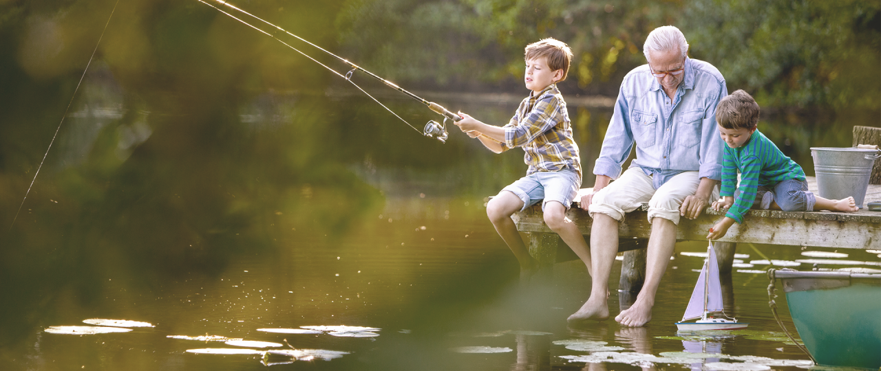 Elderly gentleman sits carefree on a footbridge and plays and fishes with his grandchildren